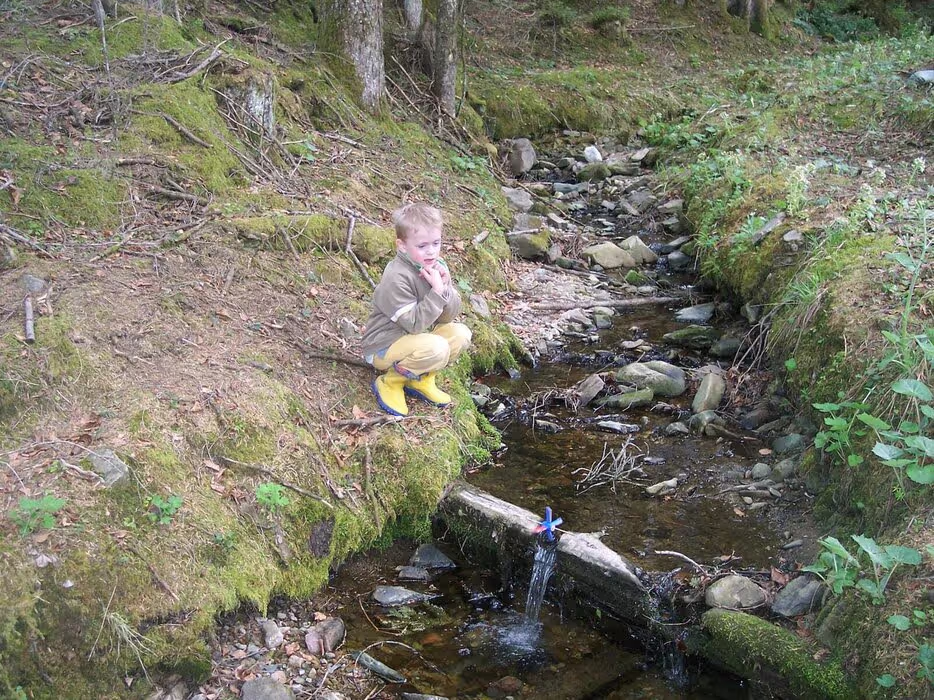 Ein Kind spielt mit seinem selbsgebauten Wasserrad am Bach