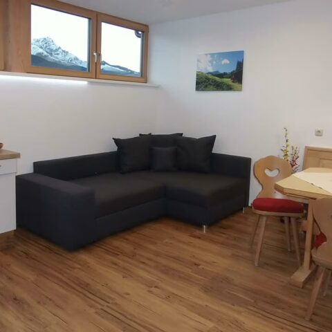 schwarze Couch, Tisch mit Blume und Aussicht auf Kitzbüheler Horn