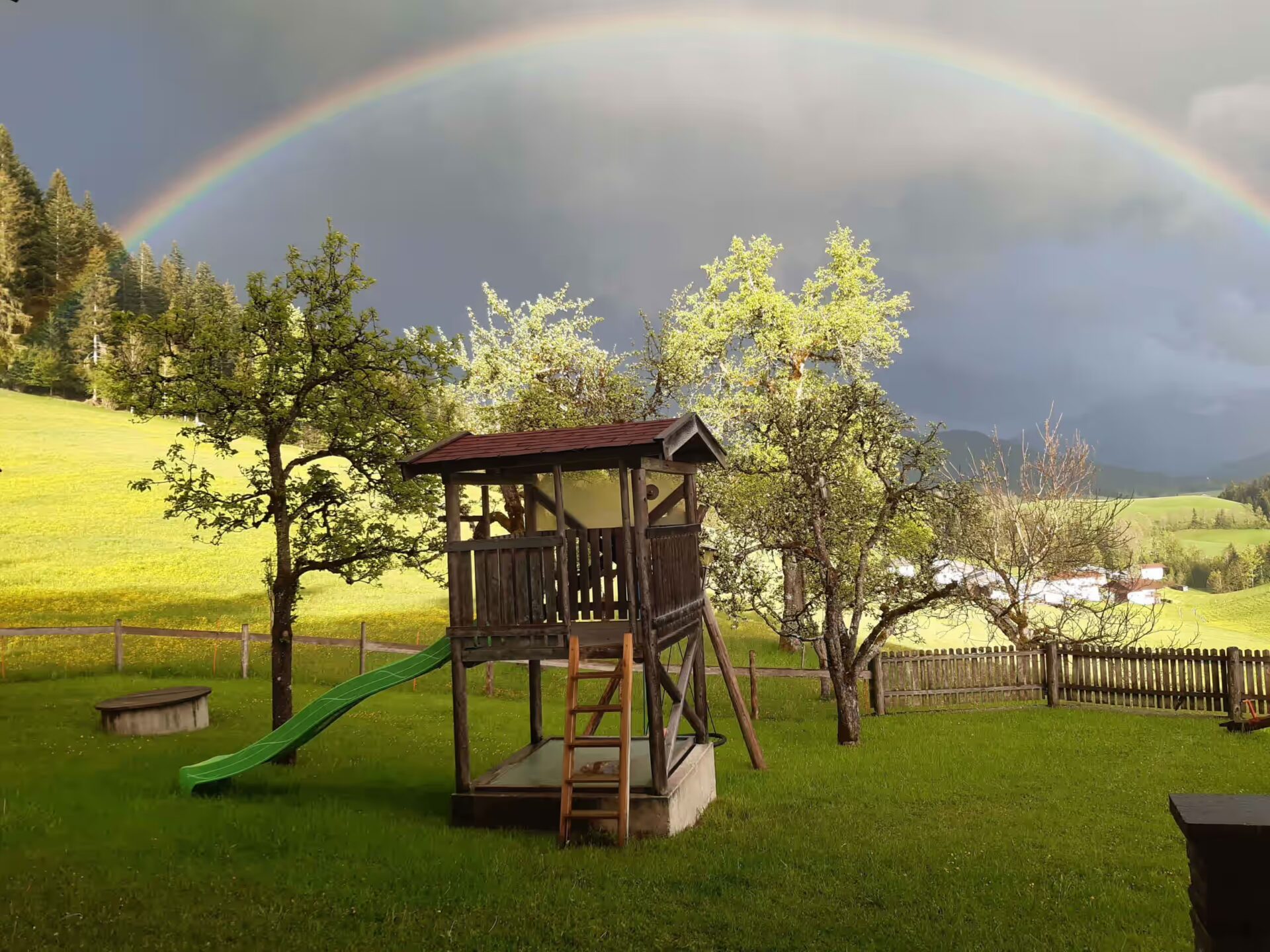 ein Regenbogen erscheint ueber dem Spielhaus, Himmel ist dunkel